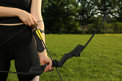 Woman with bow and arrow practicing archery in park, closeup