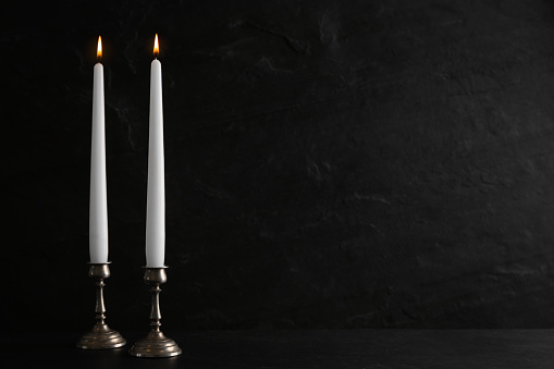 Elegant candlesticks with burning candles on black table. Space for text