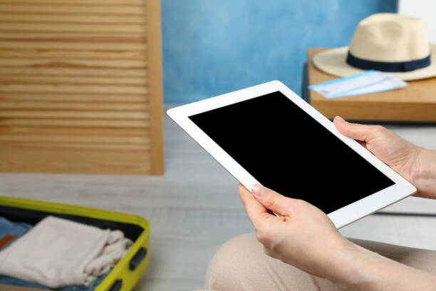 istock Woman using modern tablet while packing suitcase for summer vacation at home, closeup 1392090930