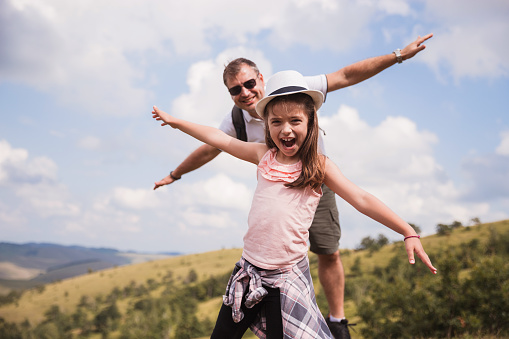 Playful father and daughter simulating flying with arms outstretched and laughing