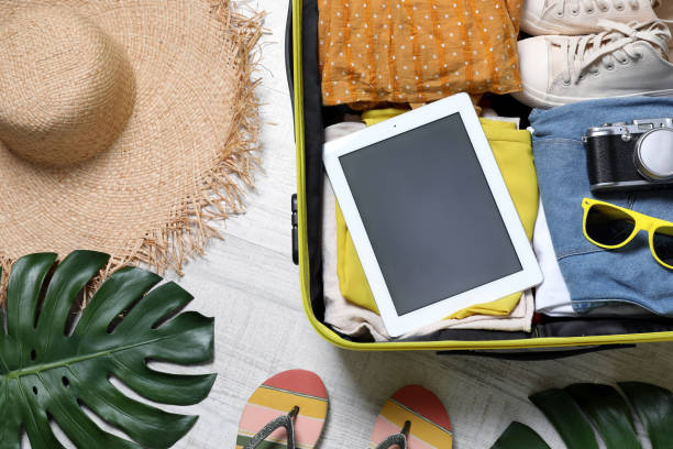 istock Packed suitcase with tablet and travel accessories on floor, flat lay. Summer vacation 1392091938