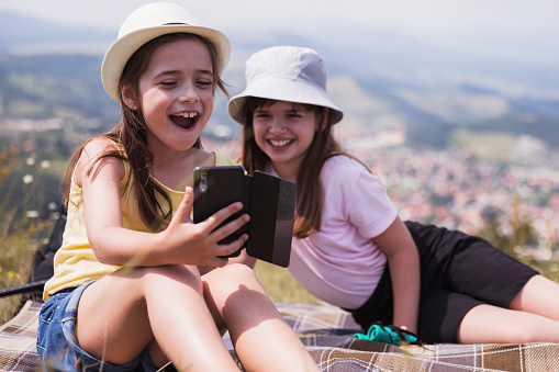 Cheerful young girls relaxing in nature and using smart phone in order to make a selfie together