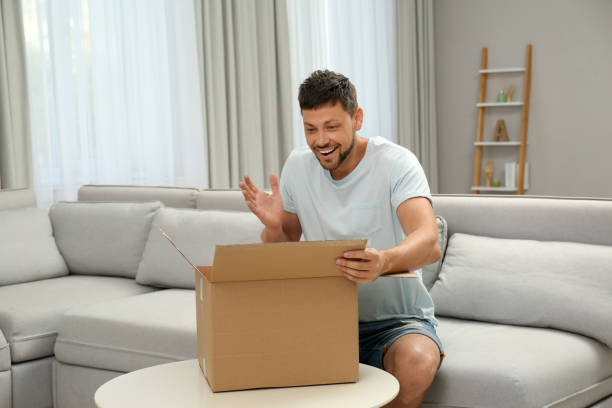 istock Happy man opening parcel on sofa at home. Internet shopping 1392094374