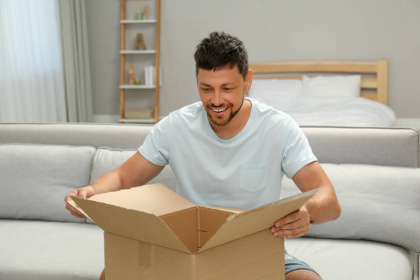 istock Happy man opening parcel on sofa at home. Internet shopping 1392094452