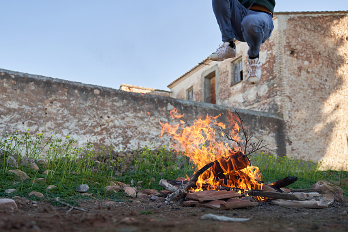 Jumping high over bonfire flames by old house in field