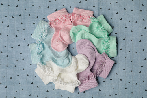 Many colorful baby socks on light blue fabric, flat lay