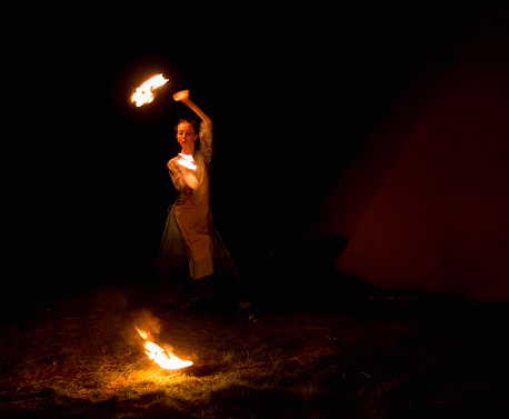 young woman doing fire show at night, motion blur of flame