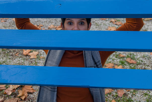 shot of a woman hidding and staring behind a blue boards