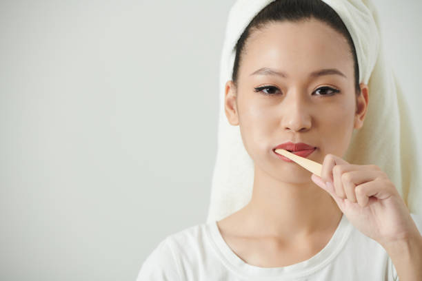 Young Woman Brushing Teeth Studio portrait of positive young woman with towel on head brushing teeth and looking at camera brushing teeth stock pictures, royalty-free photos & images