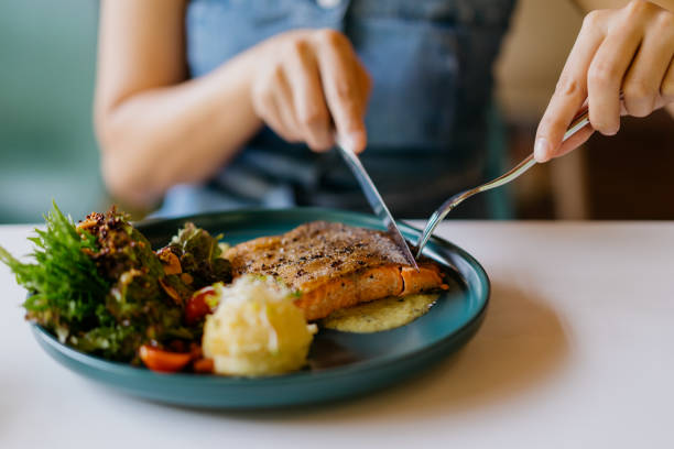 asiatische frau isst gebratenen lachs in der pfanne im café - salmon stock-fotos und bilder