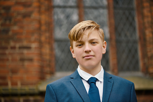 Lutheran Protestant Communion. Portrait of teenager in his confirmation suit. Fourteen year old boy standing in front of the church