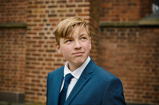 Lutheran Protestant Communion. Portrait of teenager in his confirmation suit. Fourteen year old boy standing in front of the church