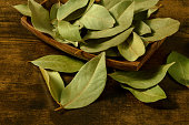 Dry bay leaves in a wooden bowl on a rustic table, a close-up