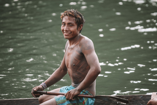 Indigenous caboclo man from an Amazon tribe in Brazil with tribal art painted on his body, riding canoe. Xingu River, Jogos Indígenas 2010.