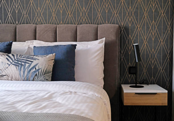 istock Close-up fragment of bedroom with empty bedside table, reading lamp and a socket in modern interior​ design home or hotel. Soft pillow and blanket, stylish comfortable furniture 1392114870