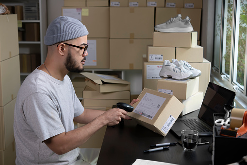 Asian man business owner scanning barcode on delivery parcel. E-commerce male business owner working in factory warehouse.