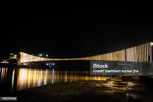 Iron Suspension Bridge Illuminated With Ferry Lights With Water Reflection From Different Angle Stock Photo - Download Image Now