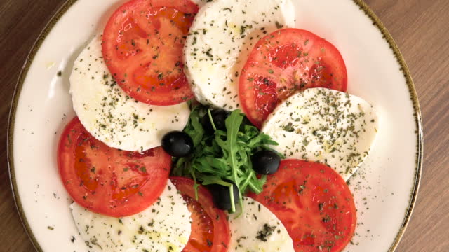 Caprese salad with ripe tomatoes and mozzarella cheese, fresh basil leaves on table background. Serbia food stock video