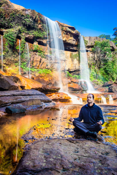istock isolated young man meditating near waterfall falling from mountain top with reflection and blue sky 1392122723
