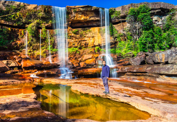 istock isolated young man sitting near waterfall falling from mountain top with reflection and blue sky 1392122851