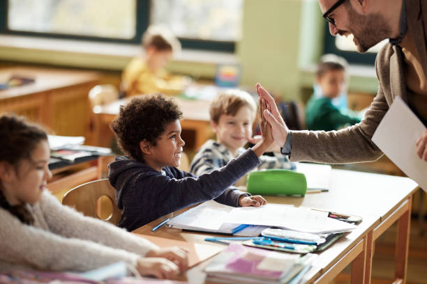 Happy teacher and schoolboy giving each other high-five on a class. Happy male teacher giving high-five to his black elementary student on a class in the classroom. schoolboy stock pictures, royalty-free photos & images