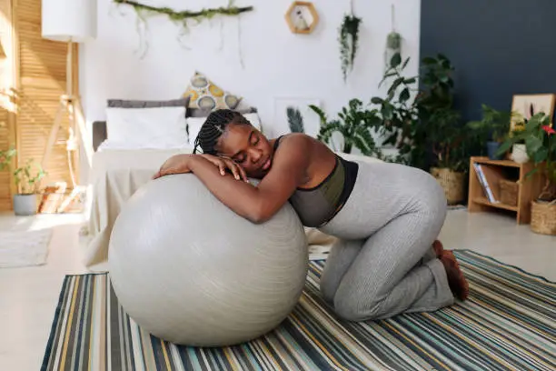 Young pregnant woman leaning on fitness ball during contractions suffering from pain