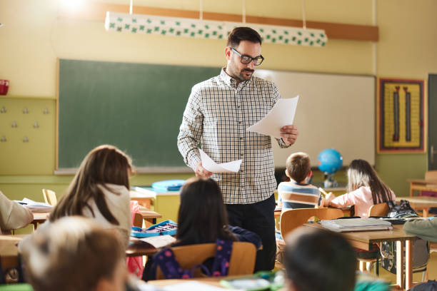 istock Young male teacher reading papers on a class in the classroom. 1392125265