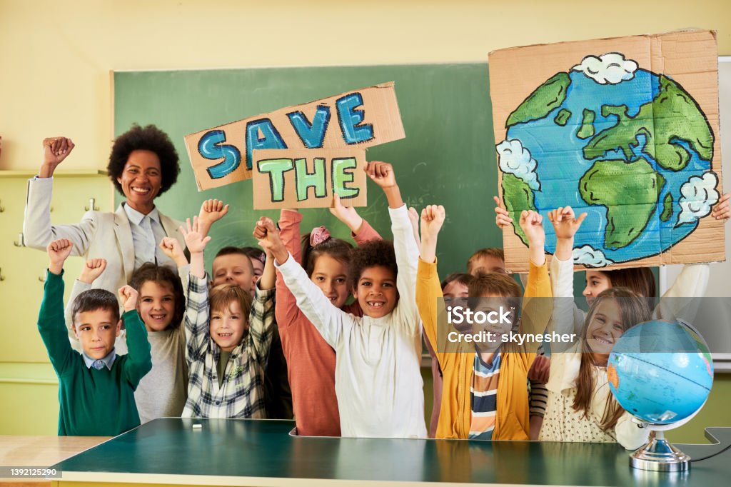 Save the Planet! Happy African American teacher and group of school kids celebrating saving of the Planet in the classroom and looking at camera. Classroom Stock Photo