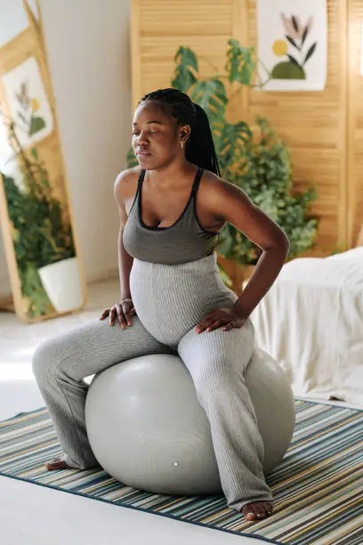 Pregnant girl sitting on fitness ball and concentrating with her eyes closed during contractions
