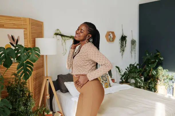 African pretty girl listening to music on her mobile phone and dancing in bedroom