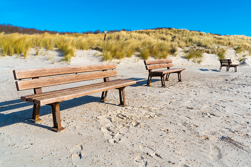 Three wooden benches on a sandy beach of the Dune island, Heligoland, Germany, on a beautiful sunny day of winter. Dunes with yellow grass in the back