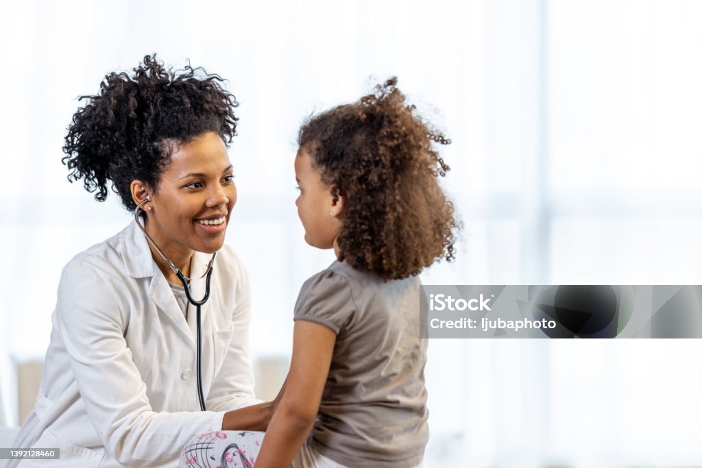 Female doctor checks girl's heartbeat A young girl sits and smiles while being seen by a middle aged female doctor. Doctor Stock Photo
