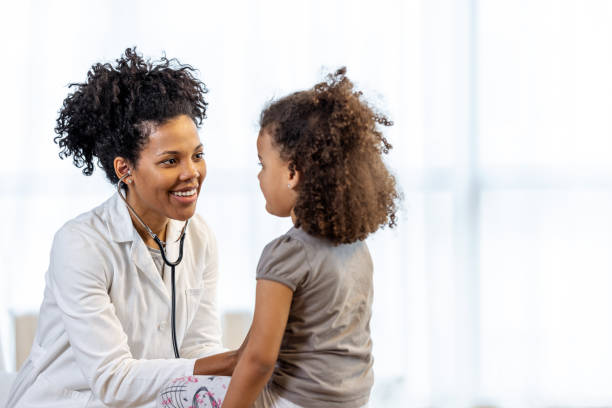 Female doctor checks girl's heartbeat A young girl sits and smiles while being seen by a middle aged female doctor. pediatrician stock pictures, royalty-free photos & images