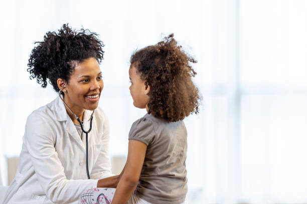 Female doctor checks girl's heartbeat A young girl sits and smiles while being seen by a middle aged female doctor. girl patient stock pictures, royalty-free photos & images