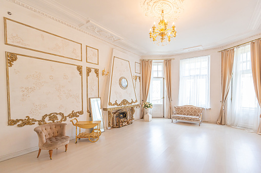 luxurious expensive interior of a large baroque royal living room. antique furniture, gold trim, huge windows, fireplace with gold stucco on the walls. full of daylight