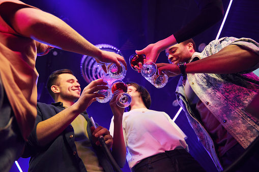 Holding glasses in hands. Group of friends having fun in the night club together.