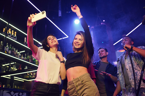 Two women making selfie. Group of friends having fun in the night club together.