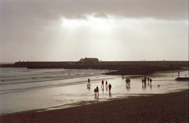 Overcast day with people wandering the beach as the tide retreats in Lyme Regis, 35mm film.