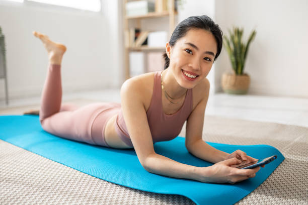 Smiling asian woman using mobile phone while relaxing after exercise workout stock photo