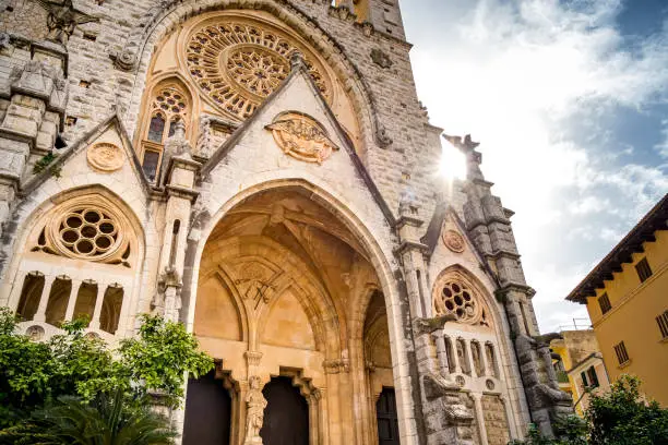 Backlit shot of the gothic revival front facade of Sant Bartomeu Church in Soller with rose window ornaments and mighty entry. Popular tourist attraction during a vacation in the village of Sóller.