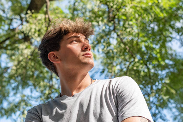 Low angle of a young man, serious, looking up under a tree