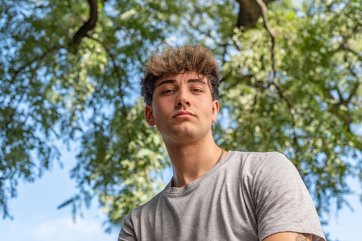 Low angle of a young man, serious, looking at the camera in a public park