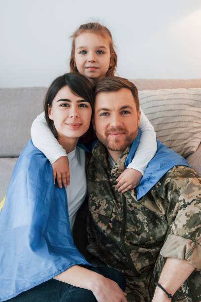 ukrainian flag is on the shoulders. soldier in uniform is at home with his wife and daughter - domestic life young family family child imagens e fotografias de stock