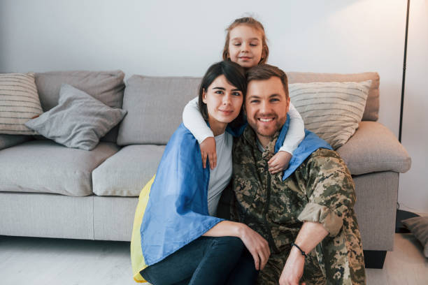 ukrainian flag is on the shoulders. soldier in uniform is at home with his wife and daughter - domestic life young family family child imagens e fotografias de stock