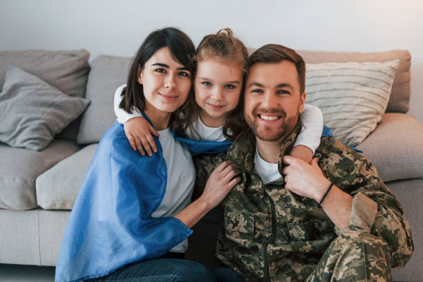 ukrainian flag is on the shoulders. soldier in uniform is at home with his wife and daughter - domestic life young family family child imagens e fotografias de stock