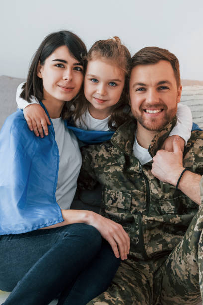ukrainian flag is on the shoulders. soldier in uniform is at home with his wife and daughter - domestic life young family family child imagens e fotografias de stock