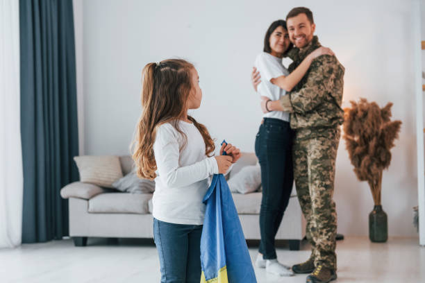 little girl holding ukraine flag. soldier in uniform is at home with his wife and daughter - domestic life young family family child imagens e fotografias de stock