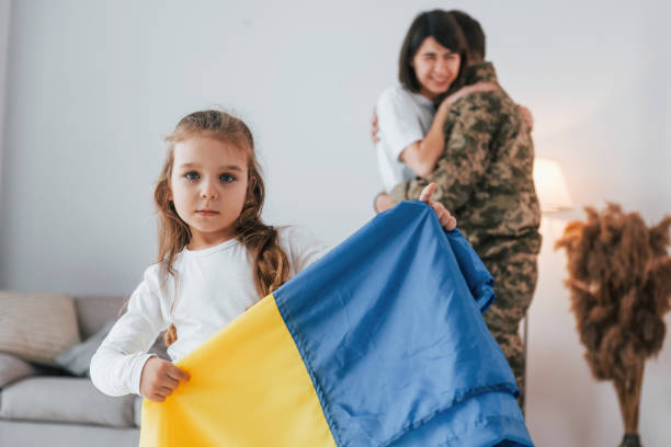 girl standing in front of her parent and holding ukraine flag. soldier in uniform is at home with his wife and daughter - domestic life young family family child imagens e fotografias de stock