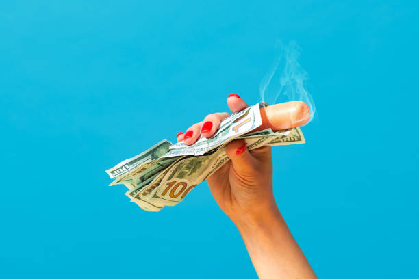 Food pop art photography. Female hand holding hot sausage wrapped in banknotes isolated on bright blue background. Vintage, retro style, surrealism, minimalism. Rich and delicious fast food. Pop art photography.Female hand holding hot sausage wrapped in banknotes isolated on bright blue background. Vintage, retro style, surrealism, minimalism. Complementary colors gift lounge stock pictures, royalty-free photos & images