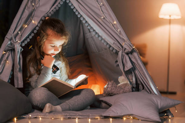 czytanie książki wieczorem. urocza dziewczynka bawiąca się w namiocie, który znajduje się w pokoju domowym - domestic tent zdjęcia i obrazy z banku zdjęć